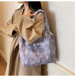 Detail of purple tie-dye tote bag with star patterns worn by model in a trench coat