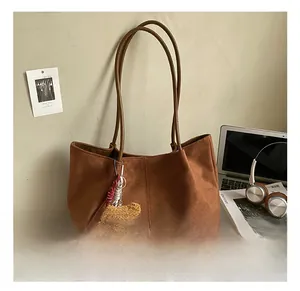 Close-up of dark brown suede tote bag with decorative bear pendant on cozy indoor background