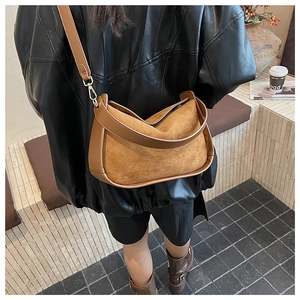Détail d'un sac bandoulière en daim marron porté avec une veste en cuir noir