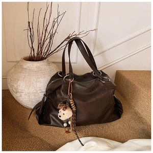 Dettaglio borsa tote in pelle marrone scuro con trama morbida e ciondolo a forma di orso