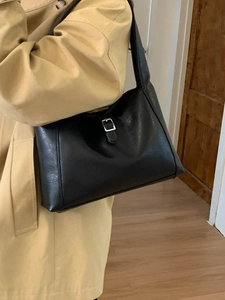 Minimalist black faux leather tote bag with silver buckle worn with a beige trench coat