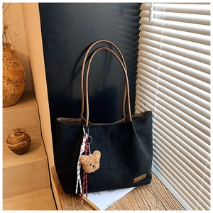 Detail of black suede tote bag with brown straps and cute bear charm in sunlight