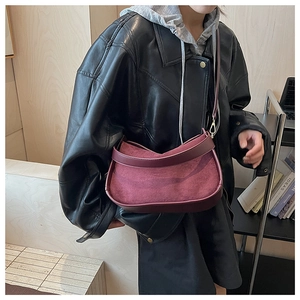 Détail d'un sac bandoulière en daim bordeaux porté par un mannequin en veste de cuir
