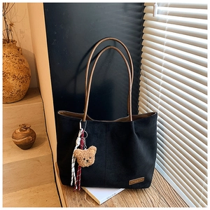 Detail of matte black suede tote bag with brown fashion tag and cute bear pendant