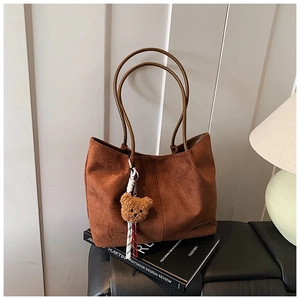 Detailed shot of caramel suede tote bag with plush bear charm and metallic brand plaque