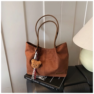 Detail of brown suede tote bag with plush bear charm on minimalist design books