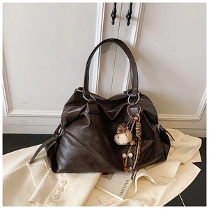 Dettaglio della borsa tote marrone scuro con cuciture diagonali e ciondolo su blazer bianco