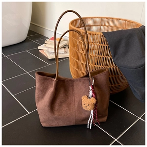 Detail of a brown suede tote bag featuring a cute plush bear pendant and leather straps