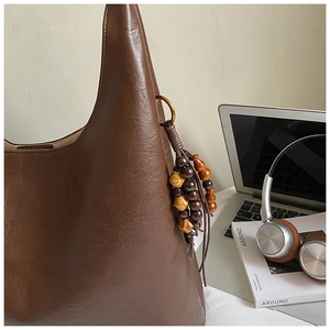 Détail d'un sac hobo en cuir marron avec un gland en perles de bois et texture douce