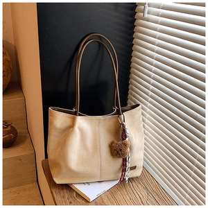 Detail of beige suede tote bag with brown handles and decorative plush bear pendant