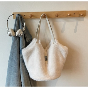 Detail view of a white plush tote bag with leather strap and metal clasp on a wooden hook