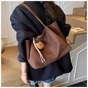 Detail of a large brown suede tote bag featuring a cute plush bear and ribbon accessory