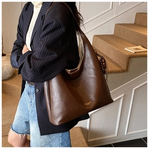 Détail d'un sac hobo en cuir marron mat avec pendentif en bois et logo de marque doré