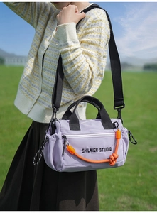 Detalle de bolso bandolera de nailon violeta claro con cuerda naranja y logo impreso