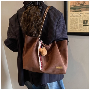 Side view of brown suede tote bag with bear charm on a model in a striped blazer