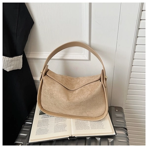 Détail du sac bandoulière en daim beige avec boucle dorée posé sur une valise