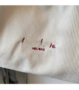 Dettaglio del tessuto in velluto a coste beige con ricamo rosso C'est la vie