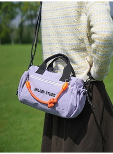 Detalle de bolso cilíndrico de nailon morado con nudo naranja y logotipo impreso
