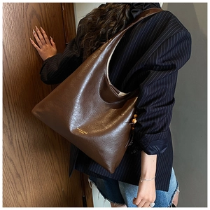 Détail d'un grand sac hobo en cuir marron avec logo doré et perles en bois décoratives