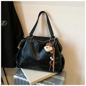 Dettaglio della borsa tote nera vintage con ciondolo a orsetto e manico in metallo