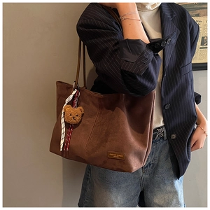 Detail view of large dark brown suede tote bag featuring bear pendant and woven strap