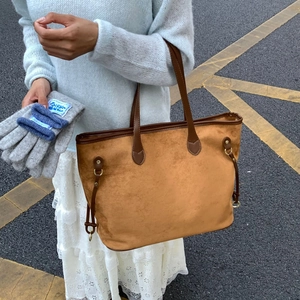 Detail of a brown suede tote bag with metal ring and grey knit gloves in use