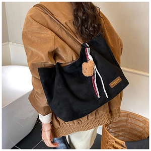 Macro detail of black suede tote bag with brown leather straps and plush bear charm