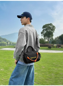 Detalle de bolso bandolera deportivo negro con decoración de cuerda naranja y logo
