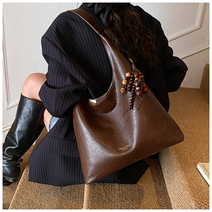 Sac fourre-tout marron avec gland en perles et logo doré dans un décor élégant