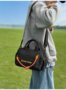 Detalle de bolso bandolera negro con cuerda naranja y bordado amarillo en primer plano