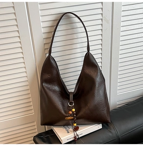Detail of dark brown vintage Hobo bag with stylish beaded tassel on black leather sofa