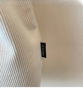 Dettaglio del tessuto in maglia a coste crema e etichetta tessuta nera con logo bianco