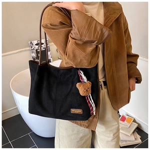 Detail of black matte suede tote bag with brown leather handles and plush bear charm