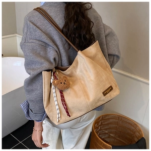 Detail of light khaki suede tote bag with brown plush bear charm and striped ribbon accent