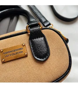 Close-up of khaki suede bag featuring black leather trim and engraved gold hardware