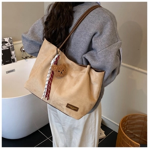 Detail of a large beige suede tote bag featuring a cute bear plush charm and woven strap