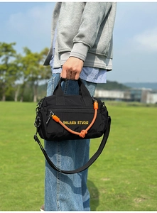 Detalle del bolso bandolera de nailon negro con nudo naranja y bordado amarillo logo