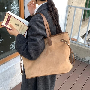 Detail of suede tote bag with brown leather handles and metallic ring hardware accents