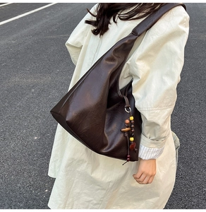 Detail view of large dark brown retro tote bag with ethnic bead charm on street model