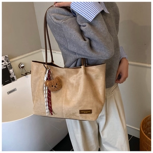 Detail of suede tote bag with brown plush bear charm and fashion label branding