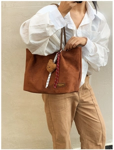 Detail of brown suede tote bag with plush bear charm and decorative rope accents