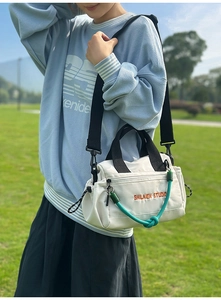 Detalle de bolso bandolera de lona blanca con logo bordado y nudo decorativo verde