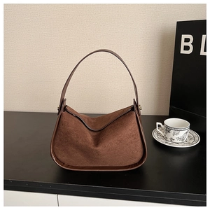 Détail du sac Hobo marron foncé en daim avec coutures en cuir lisse sur un bureau