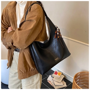 Détail du sac fourre-tout en similicuir noir avec lettrage doré et pompon en perles de bois