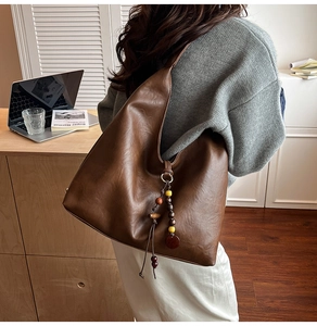 Detail of a large brown tote bag with decorative beaded tassel and leather texture