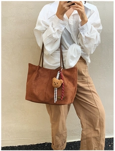 Detail of brown faux suede tote bag with teddy bear charm and woven cord on white shirt model
