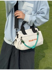 Detalle de bolso bandolera de nailon blanco con cuerda verde y bordado naranja