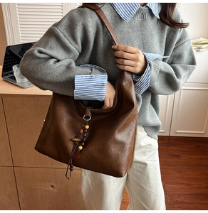 Detail view of a vintage brown leather hobo bag with unique wooden bead charm on a model