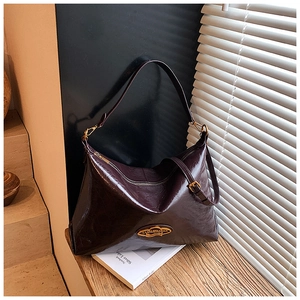Dettaglio della borsa hobo in pelle bordeaux con logo dorato su sfondo in legno