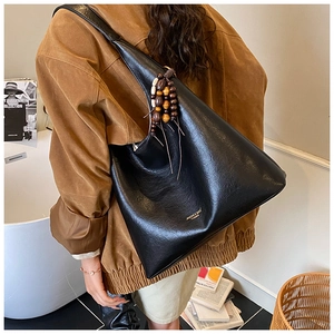 Détail d'un grand sac hobo noir avec gland en perles de bois et logo doré brillant